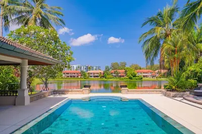 a swimming pool in front of a lake with palm trees at 4BR Lakeshore Pool Villa in Laguna Bangtao in Bang Tao Beach