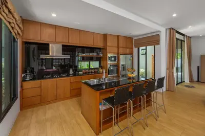 a kitchen with wooden cabinets and a bar with stools at Villa Fam with Private Pool Near Nai Harn Beach in Rawai Beach