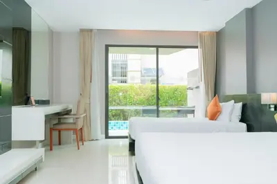 a hotel room with two beds and a desk and a window at Beachfront and Deluxe Pool Access Patong Phuket in Patong Beach