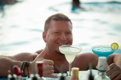 a man sitting at a pool with two cocktails at Beachfront Deluxe BR Infinity Pool Patong Phuket in Patong Beach