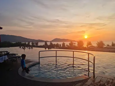 a young boy sitting in a swimming pool at sunset at Beachfront Deluxe BR Infinity Pool Patong Phuket in Patong Beach