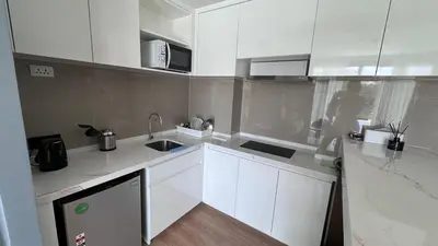 a kitchen with white cabinets and a woman standing in it at La Vita Rawai 1 Bdr Roof Pool in Rawai Beach