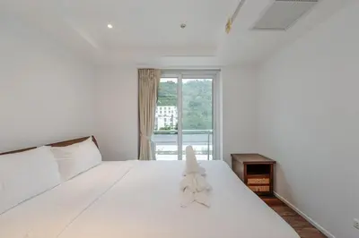 a white bed in a white room with a window at C206 Sea-View Condo 5 Min Walk to Kata Beach in Karon Beach