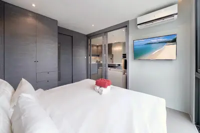 a bedroom with a white bed with a tv on the wall at Tropical & Modern Living - Hill View Tropics Kamala Suite CTG L707, Top Amenities & Beach Fun in Kamala Beach