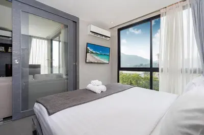 a bedroom with a large white bed and a window at Enjoy Tropics Hill Views in Kamala Suite CTG L705, Top Facilities, near FantaSea & Café Del Mar Beach Club in Kamala Beach