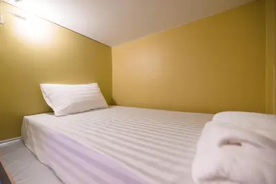 a bedroom with a white bed with a yellow wall at 113 Yellow House Hostel in Phuket Town
