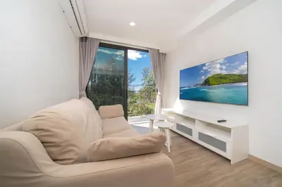 a living room with a white couch and a tv at Skypark Laguna Garden View Bang Tao Beach in Laguna Phuket