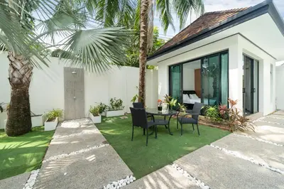 a patio with a table and chairs and palm trees at Wings Villa Laguna Bang Tao Beach Phuket in Ban Pak Lak