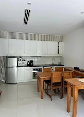a kitchen with white cabinets and a wooden table and chairs at Grand kamala falls in Kamala Beach