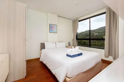 a bedroom with a white bed with a large window at LAGO APARTMENTS BY TROPICLOOK in Nai Harn Beach