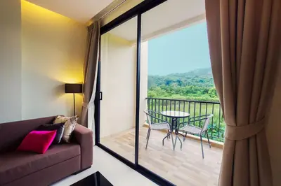 a living room with a couch and a balcony with a table at LAGO APARTMENTS BY TROPICLOOK in Nai Harn Beach