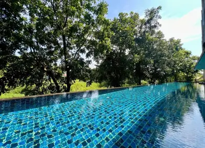 a blue swimming pool with trees in the background at Studio in Boat Avenue in Bang Tao Beach