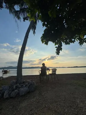 a person sitting on a chair under a tree near the water at Baan Rattana in Ko Yao Noi