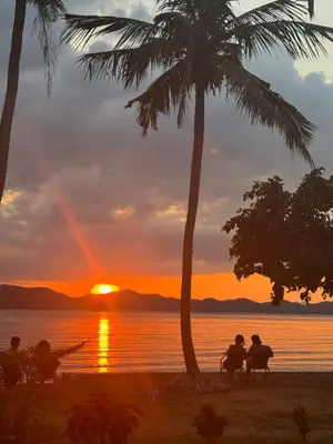 a group of people sitting under palm trees watching the sunset at Baan Rattana in Ko Yao Noi
