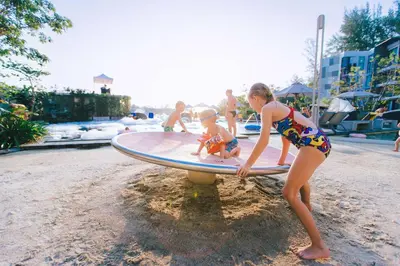 a young girl playing with a doll on a surfboard at Cassia Phuket, part of Banyan Group in Bang Tao Beach