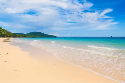 a sandy beach with the ocean and mountains in the background at Srisuksan Klong Muang Beach in Klong Muang Beach