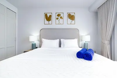 a white bed with two blue pillows on it at Beachside 1 bedroom apartment 200 meters to Bang Tao Beach Manage by OCEAN HUB in Ban Thalat Choeng Thale