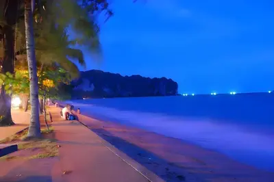 a person sitting on a bench next to a body of water at XX GO INN Aonang Beach - หาดอ่าวนาง กระบี่ in Ban Khlong Haeng