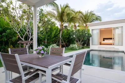 a patio with a wooden table and chairs next to a swimming pool at Trichada Tropical - 3 Bedrooms Pool Villa in Laguna Phuket