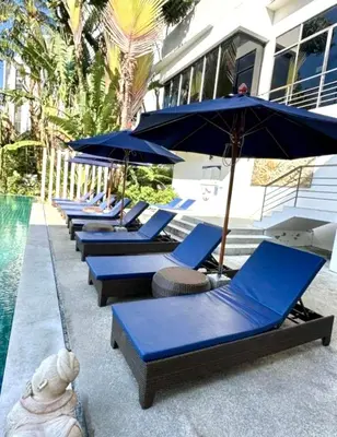a row of blue lounge chairs with umbrellas next to a pool at Veloche group in Karon Beach