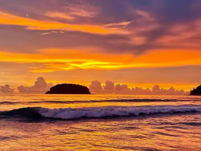 a sunset over the ocean with rocks in the water at Neptuna Kata Beach in Kata Beach
