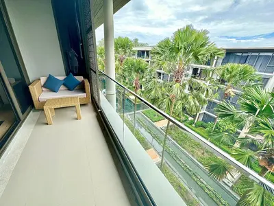 a balcony with a chair with blue pillows on it at Baan Mai Khao beachfront apartments in Mai Khao Beach