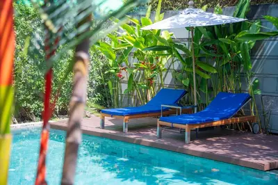 two blue chairs and an umbrella next to a pool at BangTao Anchan \u8c6a\u534e\u4e24\u5367 \u79c1\u4eba\u6cf3\u6c60 \u73b0\u4ee3\u5ea6\u5047\u5df4\u5398\u98ce in Layan Beach