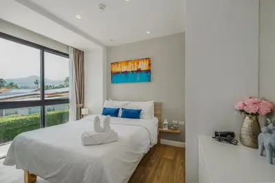 a white bedroom with a large bed and a window at Diamond Resort Phuket walk to Bangtao Beach in Phuket