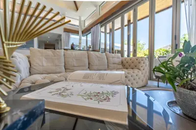 a living room with a couch and a book on a table at Botanica 4 BR Villa Layan Beach in Ban Phru Champa