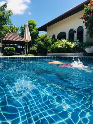 a swimming pool in front of a house with an umbrella at Green View suite with private bathroom and kitchen in Ban Phlu Yai