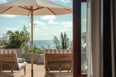 a patio with an umbrella and chairs and the ocean at Surin Ayara Villas by Stayisle in Surin Beach