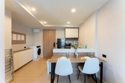 a kitchen with a wooden table and white chairs at RJ Space in Ban Thalat Choeng Thale