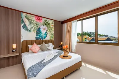 a bedroom with a bed and a large window at The Outdoor Kata Hotel in Kata Beach
