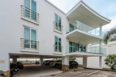 a white building with cars parked in a parking lot at C236 Best Pool &Sea View 2BR Condo Prime Location in Karon Beach