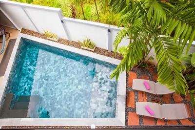 a swimming pool with two chairs and a palm tree at 150 m from a paradise beach 3 bedrooms pool in Klong Muang Beach