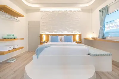 a white bedroom with a large bed with blue pillows at Stylish Studio with Pool - 8' walk to Rawai Beach - 
