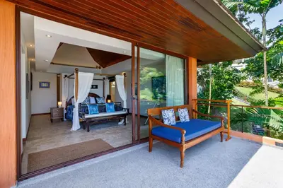 a screened in porch of a house with a blue couch and chairs at Seafront Pool Villa Nambo in Ko Taphao Noi