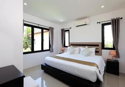 a bedroom with a large white bed with windows at RinFin Beach House - Bangtao in Ban Thalat Choeng Thale