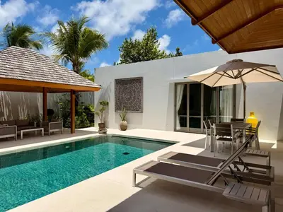 a swimming pool with chairs and an umbrella next to a house at Peaceful villa in the heart of the Anchan Tropicana project in Ban Phru Champa