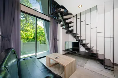 a living room with a couch and a tv and a staircase at Stylish Loft at Utopia Nai Harn great amenities in Rawai Beach