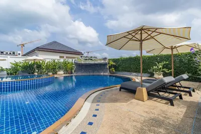 a swimming pool with two chairs and an umbrella at Bee Villa Wellness Resort Phuket in Laguna Phuket