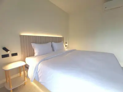 a bedroom with a large white bed and a stool at The Pinda House Bangtao in Bang Tao Beach