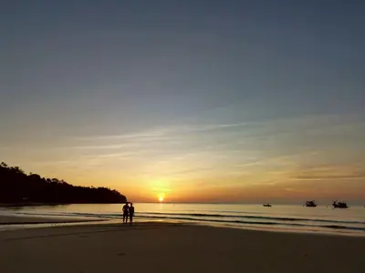 two people standing on the beach watching the sunset at The Pinda House Bangtao in Bang Tao Beach