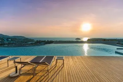 a pool with a table and chairs on a deck with the sunset at The View Phuket By RESAVA in Kata Beach