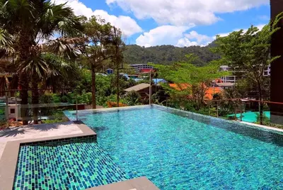 a large blue swimming pool with trees and mountains in the background at Private apartment at Emerald Terrace by Lofty in Patong Beach