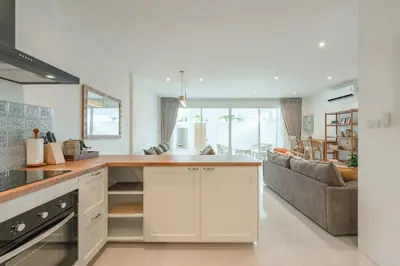 a kitchen with white cabinets and a living room at Nai Harn Beach Holiday Home - Rawai 4bdr in Rawai Beach