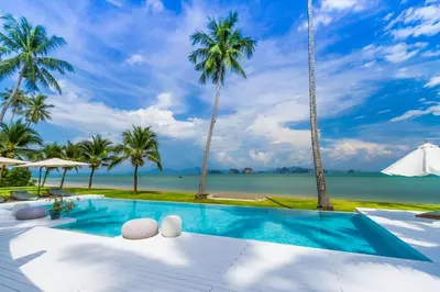 a swimming pool with palm trees and the ocean at Baan Klong III in Ko Yao Noi