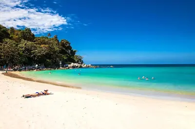a woman laying on a beach with people in the water at 1 BR Suite 8-198 at Ozone Condo near Kata beach and surf in Kata Beach