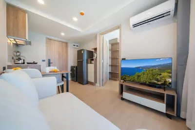 a living room with a large tv and a kitchen at Cosy 1 bedroom apt at Space Cherngtalay - 402 in Bang Tao Beach