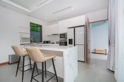 a kitchen with white walls and a counter with stools at Nicky Luxury Private Pool Villa in BangTao Laguna in Laguna Phuket